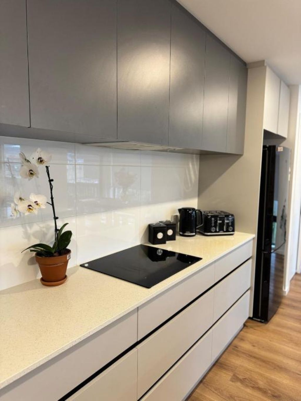 Une cuisine moderne avec des meubles gris, un plan de travail noir, une cuisinière encastrée et une orchidée en pot.