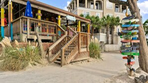Une maison de plage en bois, dotée d’un porche, d’un escalier et d’un panneau indicateur indiquant plusieurs directions.
