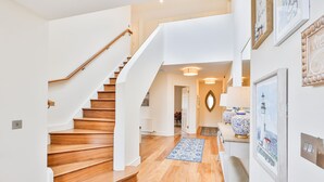 Una escalera con escalones de madera y paredes blancas que conduce a un pasillo con una puerta blanca y un tapete azul con estampado.