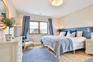 Een slaapkamer met een bed, nachtkastje, kaptafel en een raam met gordijnen.