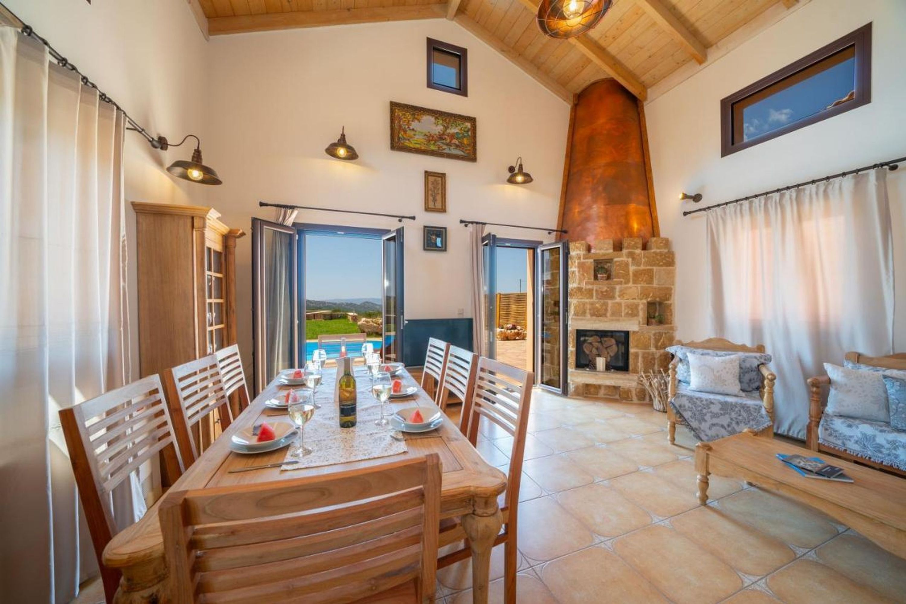Un coin repas avec une table dressée pour quatre personnes, une cheminée en pierre et une vue sur l’extérieur.
