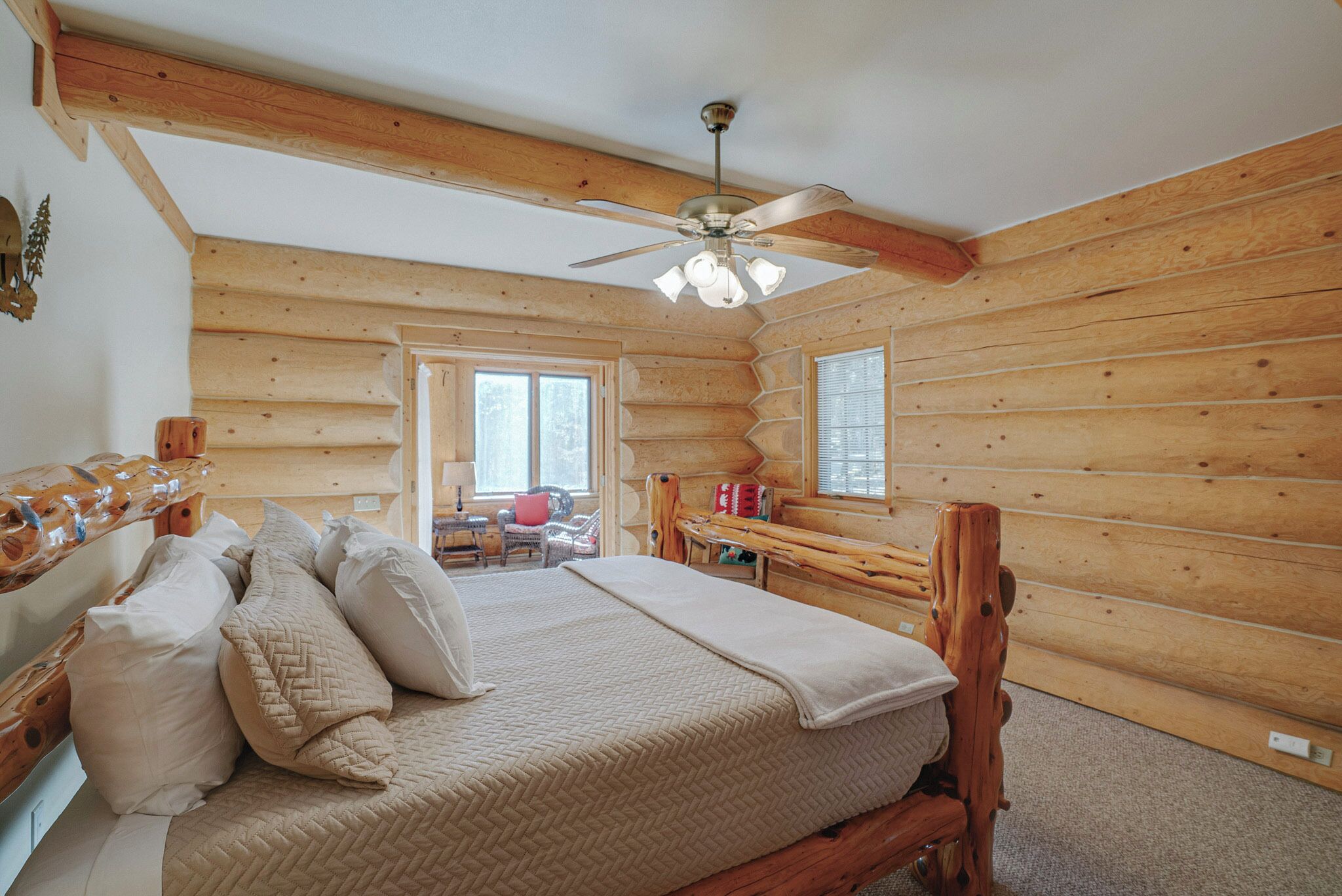 A log cabin bedroom with a wooden bed, a ceiling fan, and a window.
