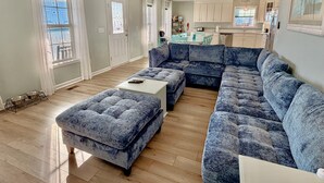 A living room with a sectional sofa, ottoman, and a small table. - Oceanview retreat in Oak Island, sleeps 12, perfect for families and a dog! (Oak Island)