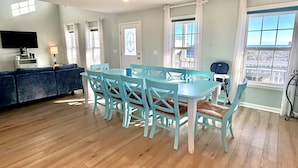 A dining area with a table and chairs, a sofa, a TV, and a window with a view. - Oceanview retreat in Oak Island, sleeps 12, perfect for families and a dog! (Oak Island)