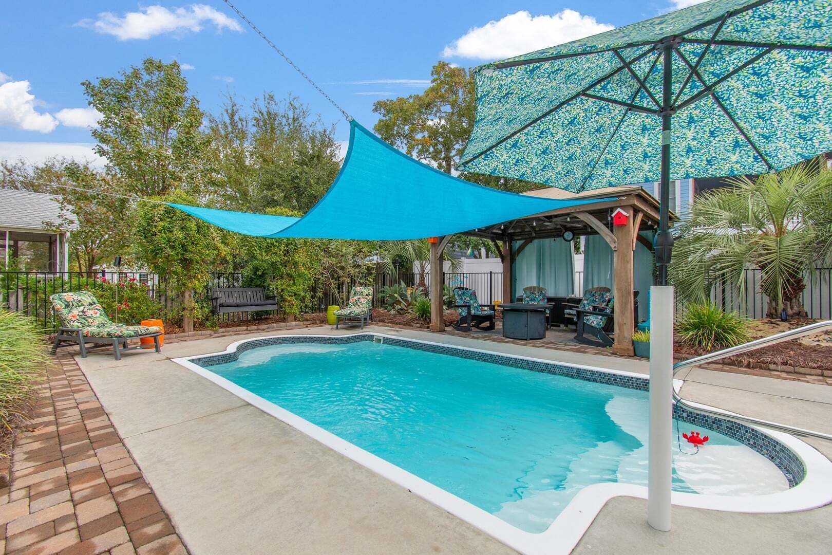 Un patio trasero con piscina, mobiliario de jardín y una zona de estar cubierta.