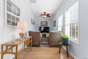 A cozy living room with a TV, wicker chairs, a wooden table, and a ceiling fan. - Nemo's Place: Spacious 4BR retreat with private pool in scenic Oak Island. (Oak Island)
