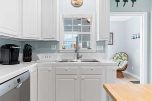 A kitchen with white cabinetry, a stainless steel sink, and a window above the counter. - Nemo's Place: Spacious 4BR retreat with private pool in scenic Oak Island. (Oak Island)