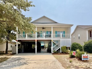A two-story house with a covered front porch, a balcony, and a staircase leading to the upper level. - Nemo's Place: Spacious 4BR retreat with private pool in scenic Oak Island. (Oak Island)
