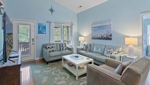 A living room with two sofas, a coffee table, and a lamp. There is a door with a window, and a painting on the wall. - Nemos II: A charming 3BR retreat in Oak Island, perfect for family getaways. (Oak Island)