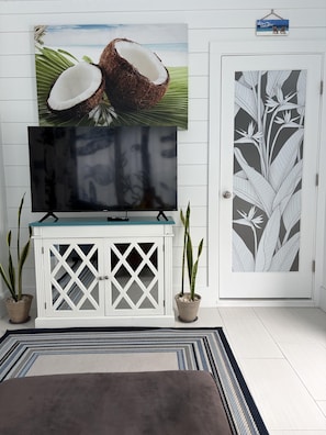 A flat-screen TV on a white cabinet with a tropical-themed wall art above it. - Nemos II: A charming 3BR retreat in Oak Island, perfect for family getaways. (Oak Island)