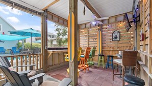 A covered outdoor seating area with wooden furniture, a surfboard, and a 'Welcome' sign. - Nemos II: A charming 3BR retreat in Oak Island, perfect for family getaways. (Oak Island)