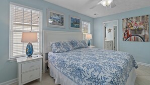 A bedroom with a bed, two bedside tables, a ceiling fan, and artwork on the walls. - Nemos II: A charming 3BR retreat in Oak Island, perfect for family getaways. (Oak Island)