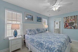A bedroom with a bed, two bedside tables, a ceiling fan, and artwork on the walls. - Nemos II: A charming 3BR retreat in Oak Island, perfect for family getaways. (Oak Island)