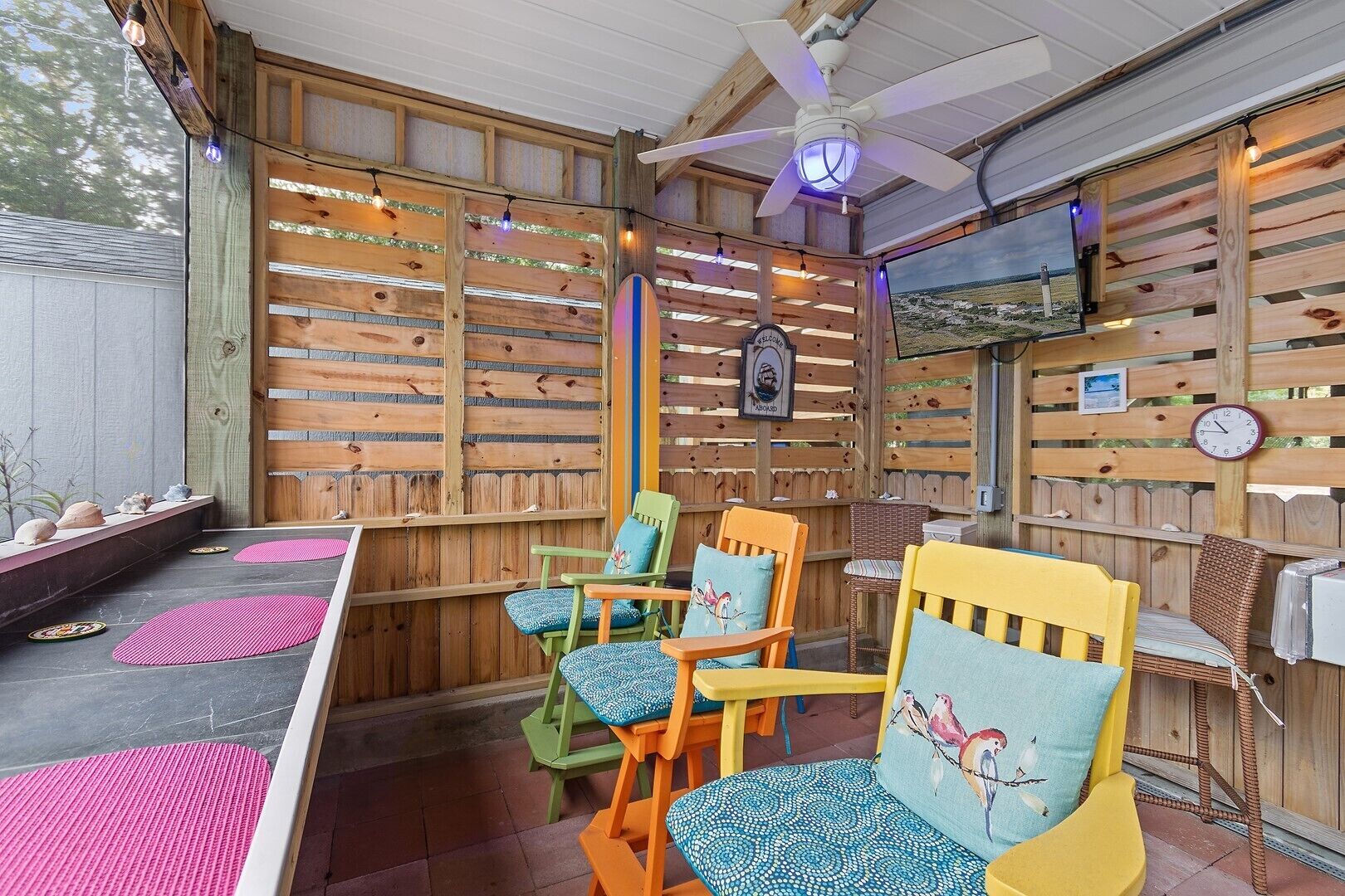 A covered patio area with wooden walls, a ceiling fan, and a television screen.