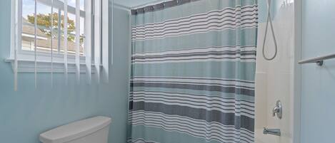 A bathroom with a toilet, a shower with a striped curtain, and a window with blinds.