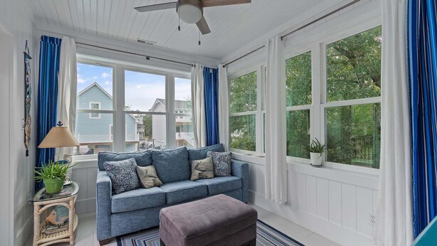 A sunroom with a blue sofa, a ceiling fan, and large windows. - Nemos II: A charming 3BR retreat in Oak Island, perfect for family getaways. (Oak Island)