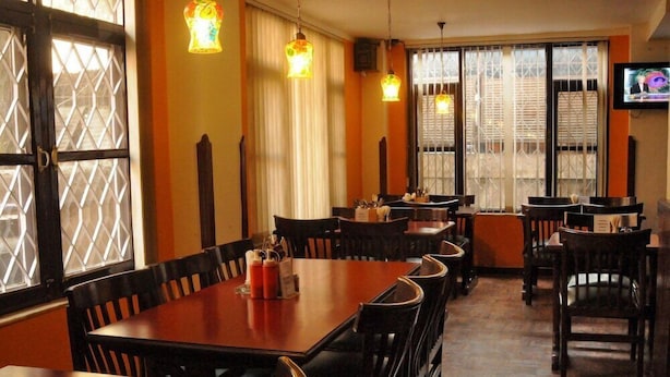 A restaurant with wooden tables and chairs, warm lighting, and a television on the wall. - Hotel Excelsior Ltd (Kathmandu)