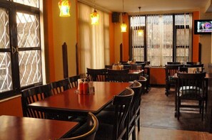 A restaurant with wooden tables and chairs, warm lighting, and a television on the wall. - Hotel Excelsior Ltd (Kathmandu)