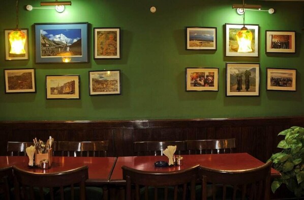 A restaurant with wooden tables and chairs, framed pictures on the walls, and a green wall. - Hotel Excelsior Ltd (Kathmandu)