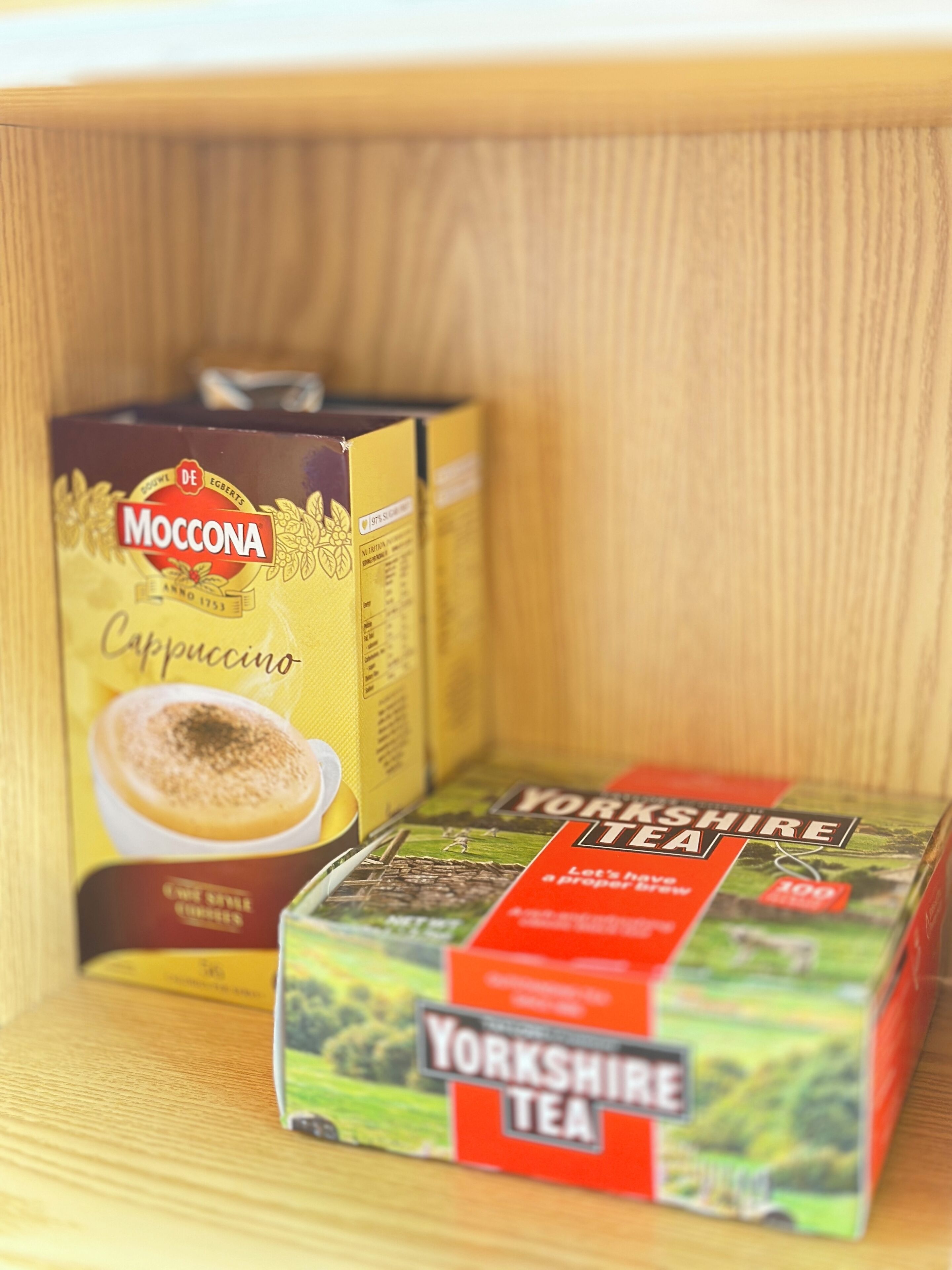 Two boxes of Moccona Cappuccino and Yorkshire Tea on a wooden shelf.