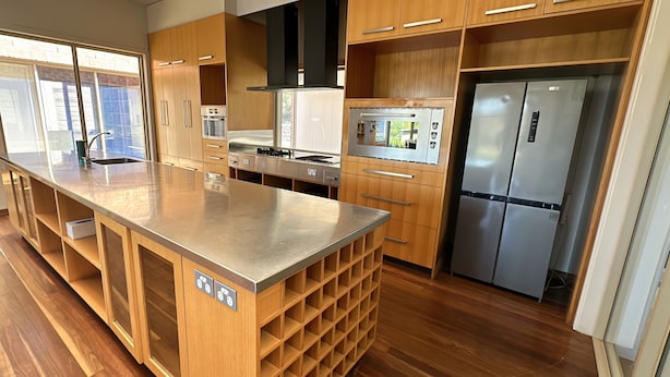 A modern kitchen with wooden cabinets, a stainless steel island, built-in appliances, and a large window. - Return to nature (Putty)