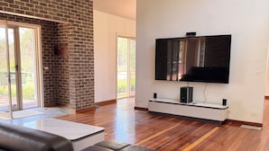 A modern living room with a brick fireplace, a large flat-screen TV, and a ceiling fan. - Return to nature (Putty)