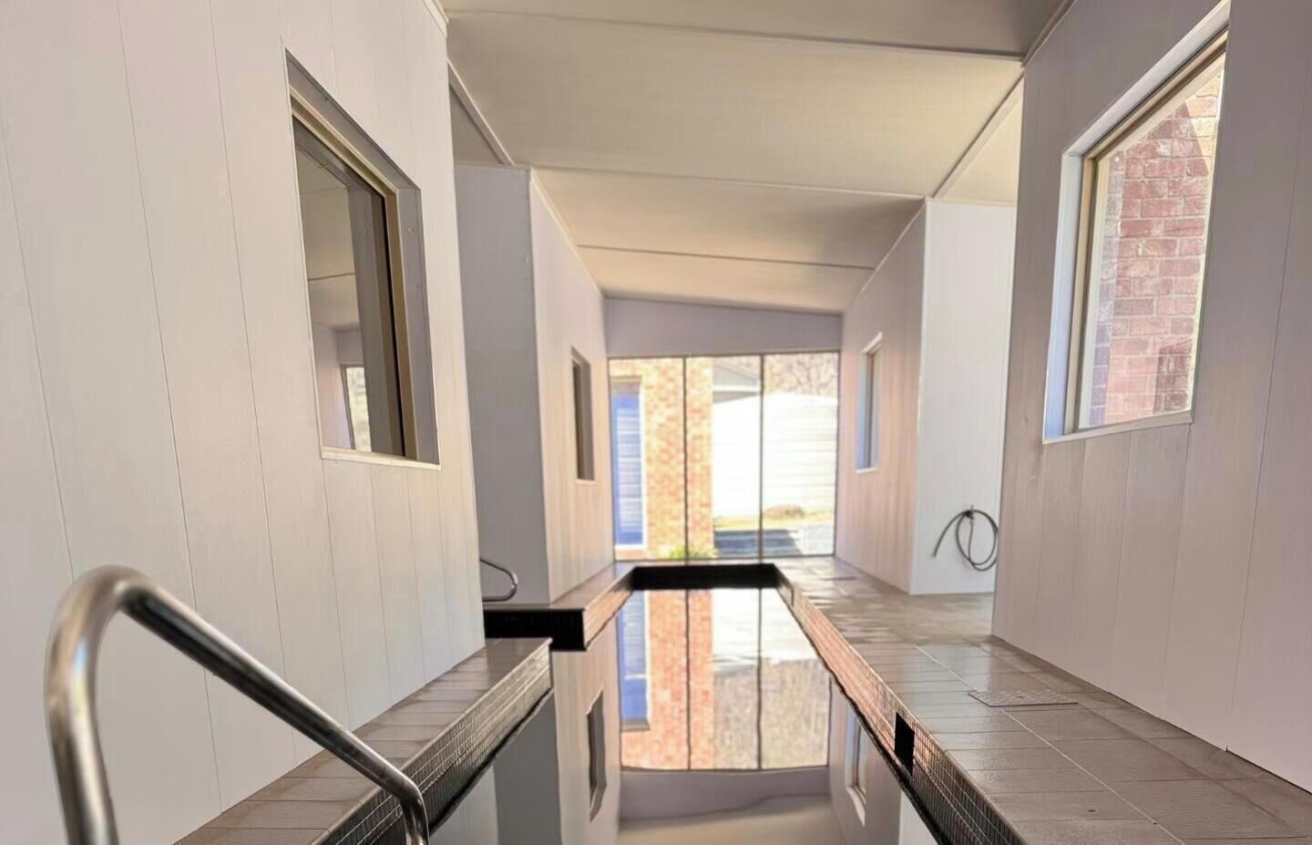 A modern hallway with a glass partition, metal railings, and large windows.
