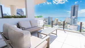 Ein Balkon mit einer Couch und einem Tisch, mit Blick auf eine Stadtlandschaft und das Meer.