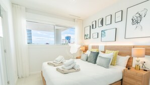 Ein modernes Hotelzimmer mit einem großen Bett, ordentlich gefalteten Handtüchern, einem hölzernen Kopfteil, einem Nachttisch mit Lampe und gerahmten Kunstwerken an der Wand.