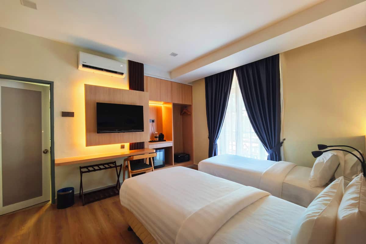 Una habitación de hotel con dos camas, un escritorio con una silla, un televisor y una ventana con cortinas.