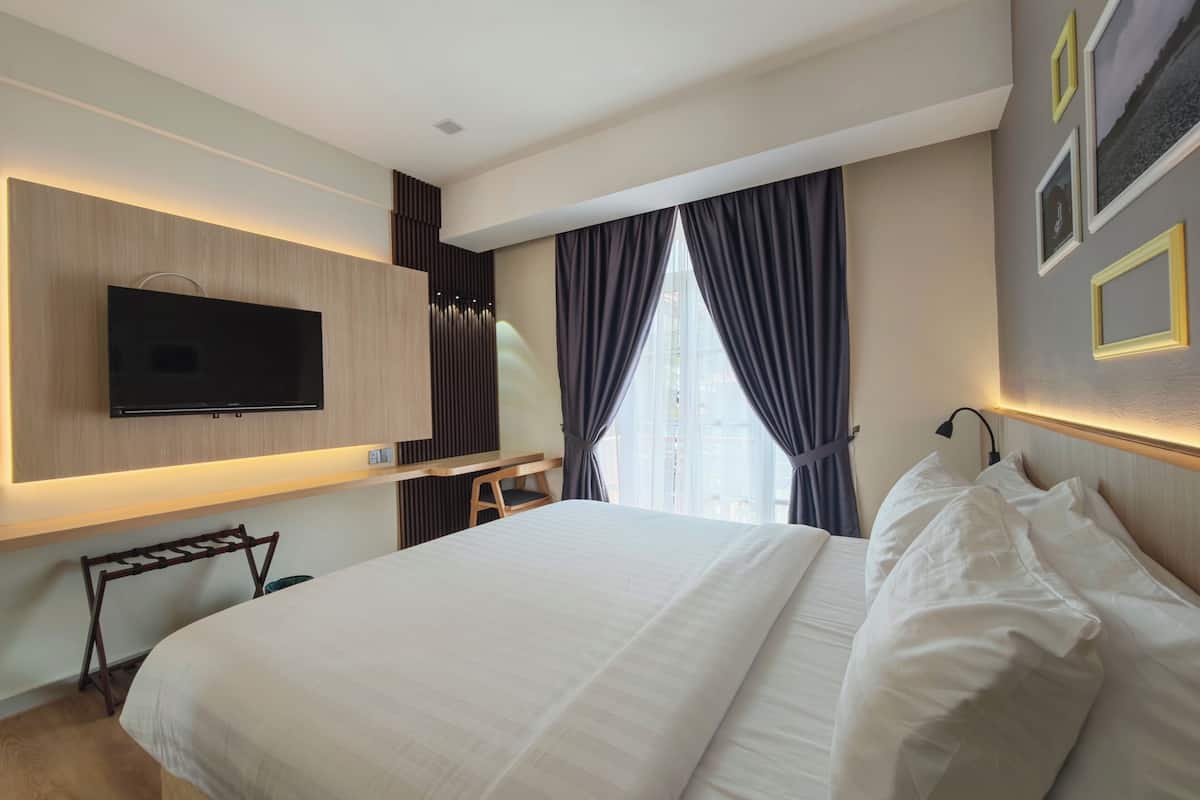 Una habitación de hotel moderna con una cama grande, un televisor de pantalla plana montado en la pared, un escritorio con una silla y una ventana con cortinas.