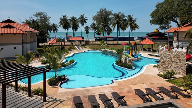 A resort pool with a curved design, palm trees, and a view of the ocean. - Raia Beach Resort Port Dickson (Port Dickson)