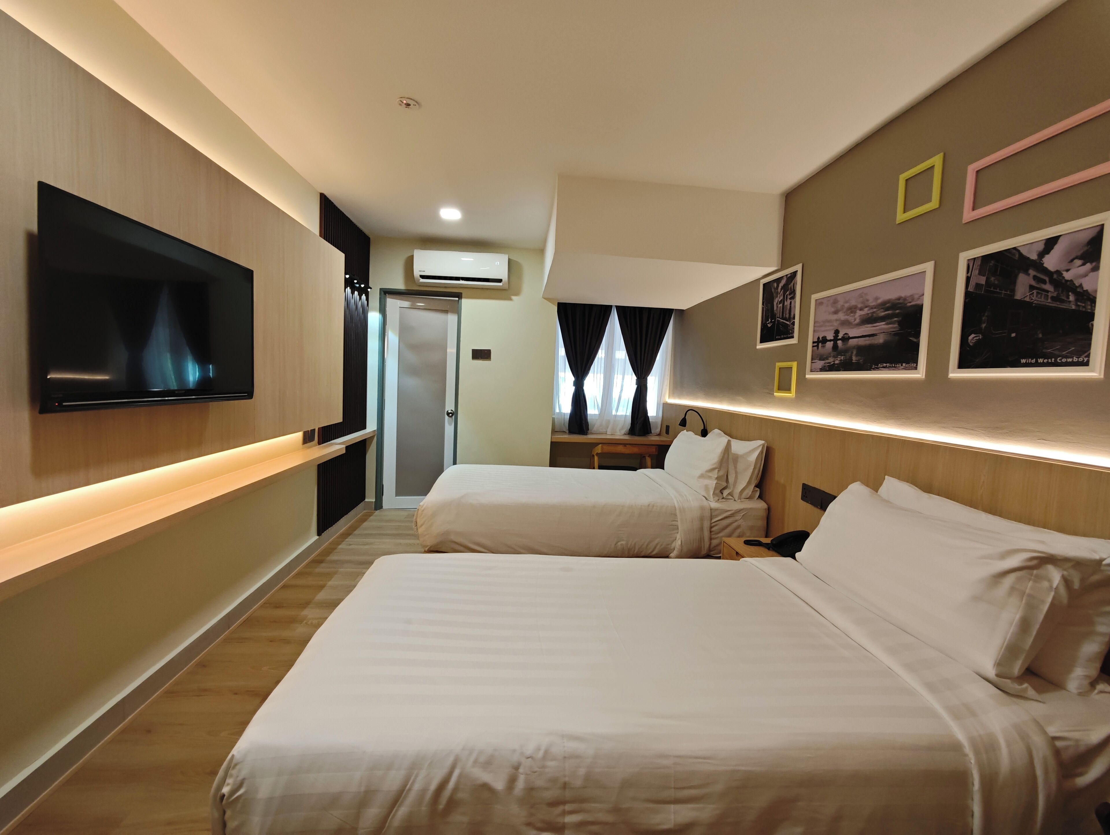 Habitación de hotel con dos camas, un televisor montado en la pared, un equipo de aire acondicionado y cuadros enmarcados.