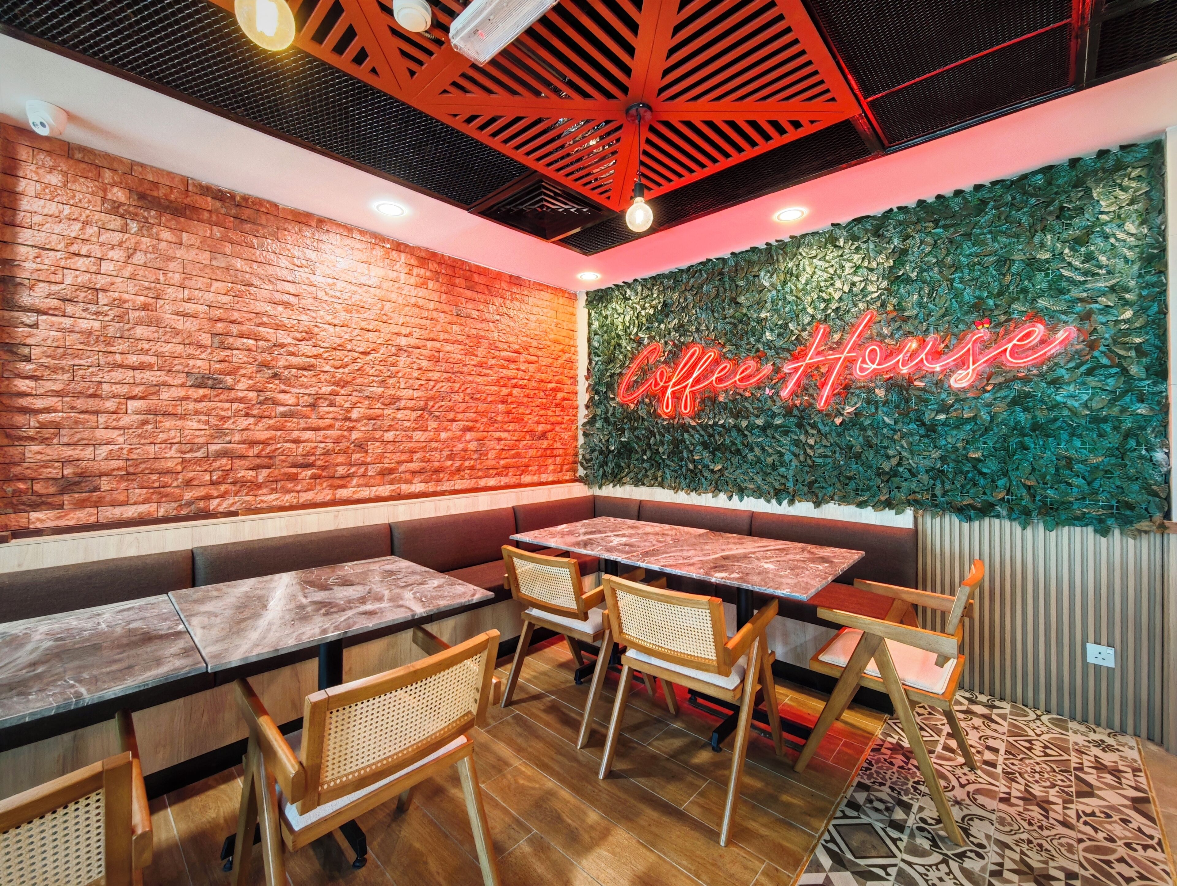 A cozy cafe interior with brick walls, wooden tables, and a neon sign reading "Coffee House".