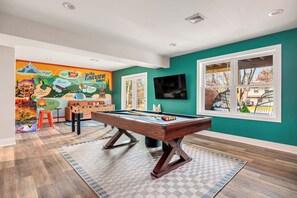 Een pooltafel in een ruimte met blauwgroene muren, een muurschildering en een raam met uitzicht.