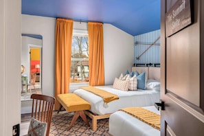 Een hotelkamer met een bed, een bankje, een stoel, een raam met gordijnen en uitzicht op het omliggende landschap.