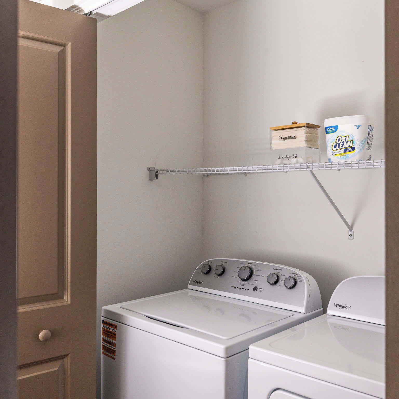 A laundry room with a Whirlpool washer and dryer, a shelf with laundry detergent, and a metal drying rack.