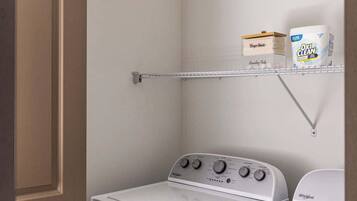 A laundry room with a Whirlpool washer and dryer, a shelf with laundry detergent, and a metal drying rack.