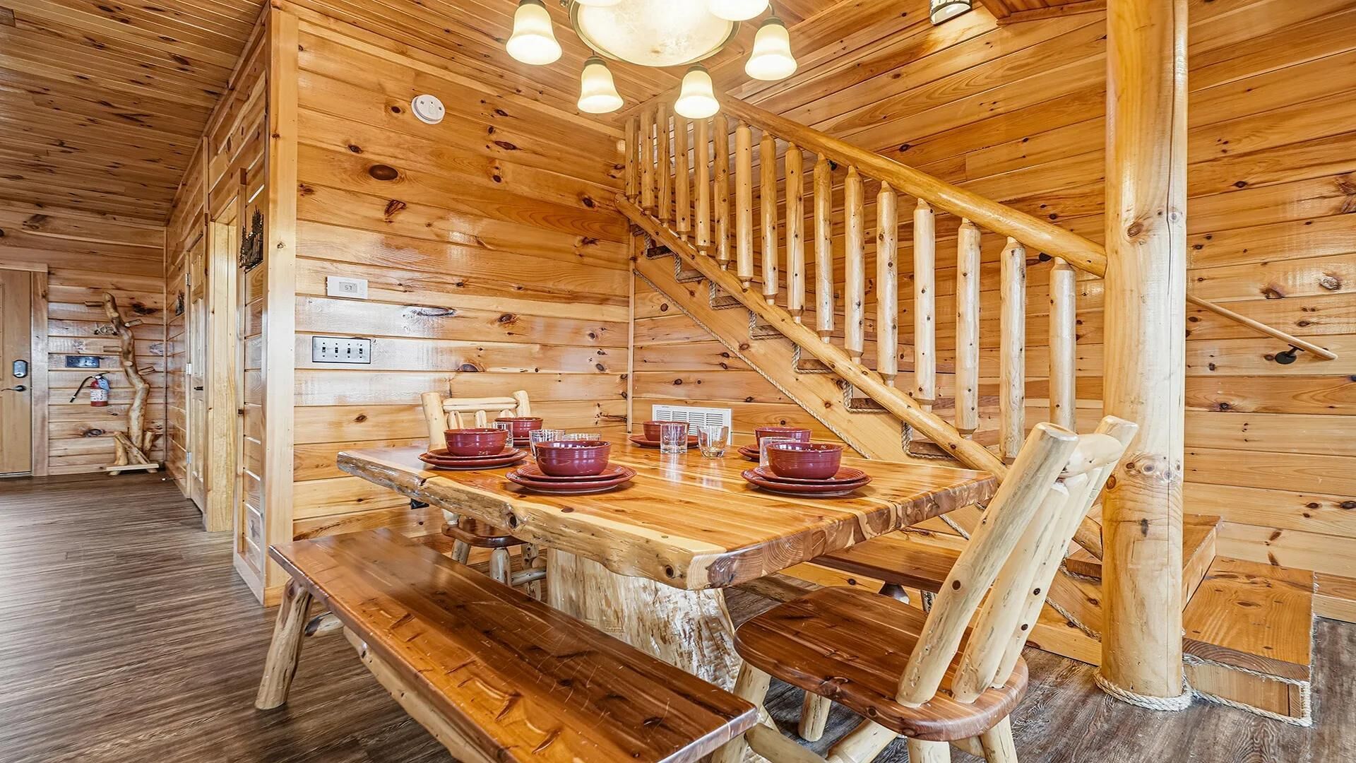 A wooden interior with a dining table set for four, a wooden bench, and a spiral staircase.