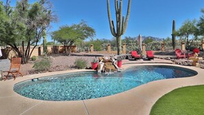 A pool with a waterfall feature, surrounded by desert vegetation and cacti. - Canyon Ridge Oasis (Tucson)