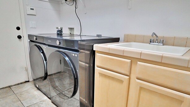 A compact kitchen with a built-in washer and dryer, a sink, and light-colored cabinets. - Canyon Ridge Oasis (Tucson)