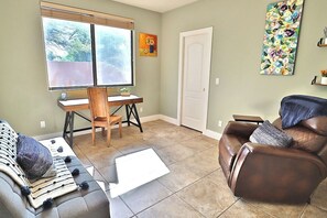 A living room with a sofa, a recliner, a desk with a chair, and a window with blinds. - Canyon Ridge Oasis (Tucson)