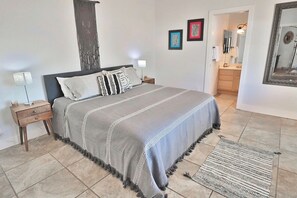 A bedroom with a bed, bedside tables, a rug, and a bathroom visible through an open door. - Canyon Ridge Oasis (Tucson)