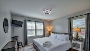 Un dormitorio con cama, escritorio, televisor y ventana con cortinas.