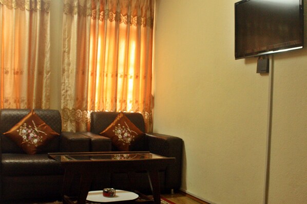 A living room with a sofa, a coffee table, and a television mounted on the wall. - Hotel The Greatwall (Kathmandu)