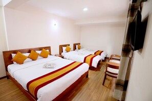 Une chambre d’hôtel avec trois lits, chacun doté de draps blancs et d’oreillers jaunes. On y trouve une chaise en bois et un téléviseur fixé au mur.