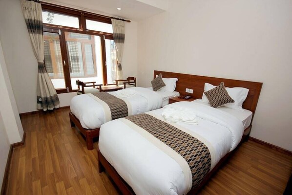 A hotel room with two beds, wooden flooring, and a large window with curtains. - Hotel Holiday House Kathmandu (Kathmandu)