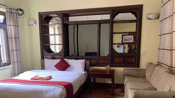 A hotel room with a wooden bed, a small bedside table, a sofa, and a large mirror with a decorative frame. - Potala Tourist Home (Kathmandu)