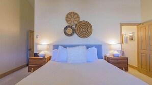 A bedroom with a large bed, two bedside tables, and a headboard. There are three wall decorations above the bed. - Updated Treasury Point condo, garage, hot tub! (Crested Butte)