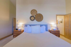 A bedroom with a large bed, two bedside tables, and a headboard. There are three wall decorations above the bed. - Updated Treasury Point condo, garage, hot tub! (Crested Butte)